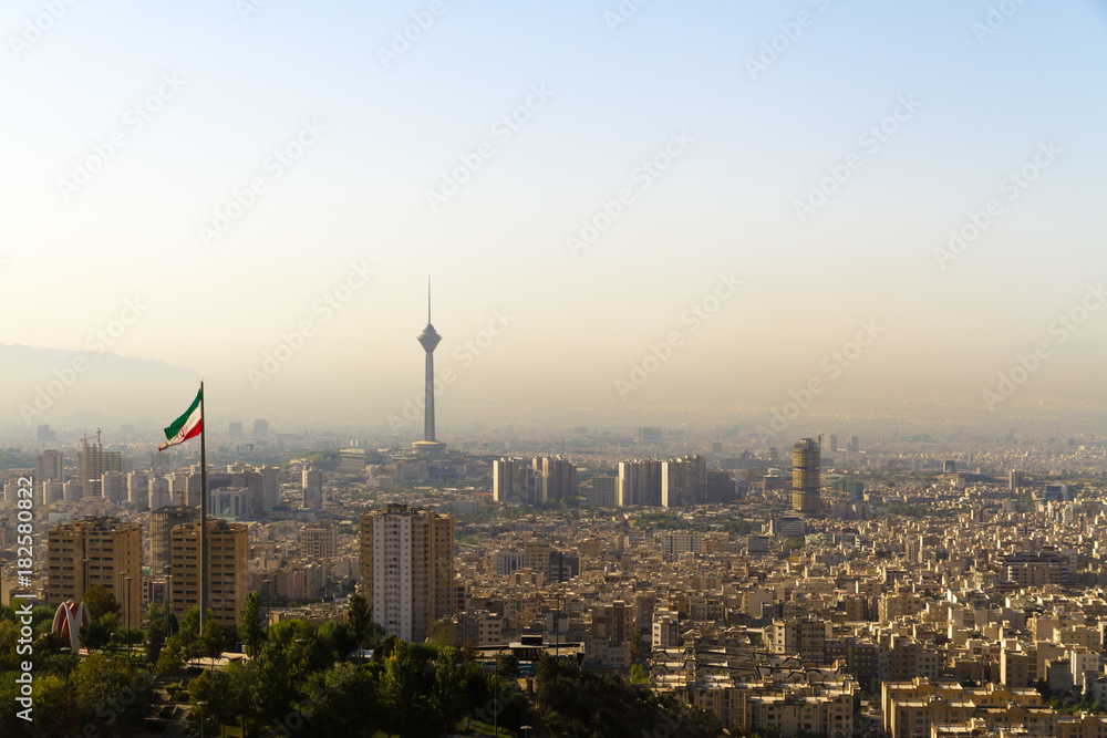 Tehran city skyline with Iranian flag and Milad Tower (Borj-e Milad landmark, hight 435 m.), seen from northern Tehran. Due to heavy traffic this capital suffers from a yellow layer of smog.