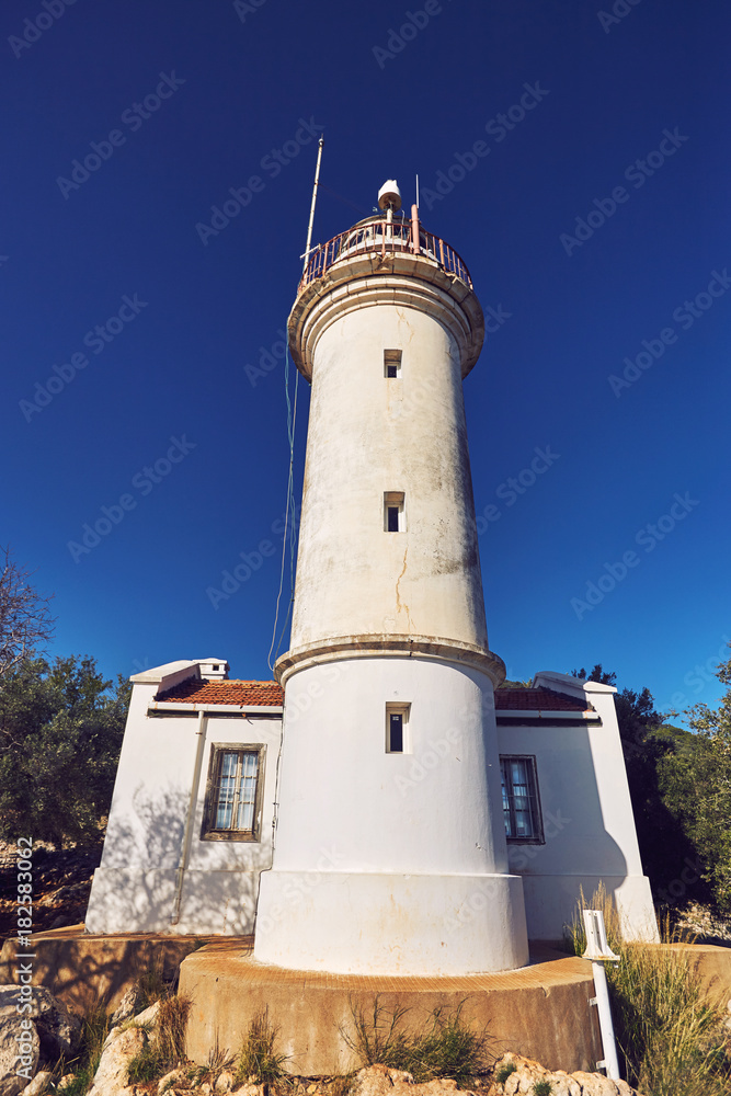 A white lighthouse indicating the path on the seashore under the sky.