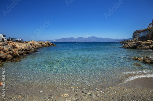 A calm marine landscape with mountains under a clear blue sky