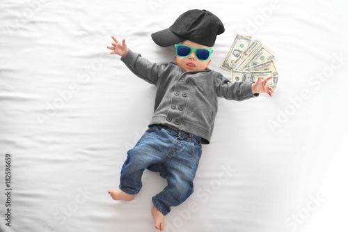 Cute boy with money on white bedsheet