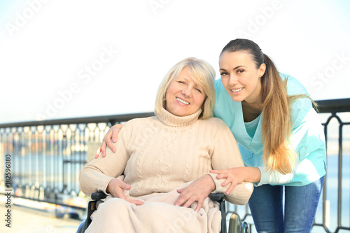 Disabled senior woman and young caregiver outdoors © Africa Studio