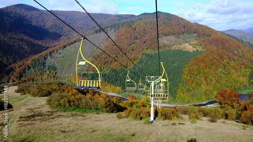 4K UHD footage of ski lift or elevator going down with empty seats over colorful autumn mountain landscape background photo