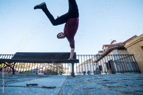 Young man doing handstand on a bench in the street while doing parkour. 