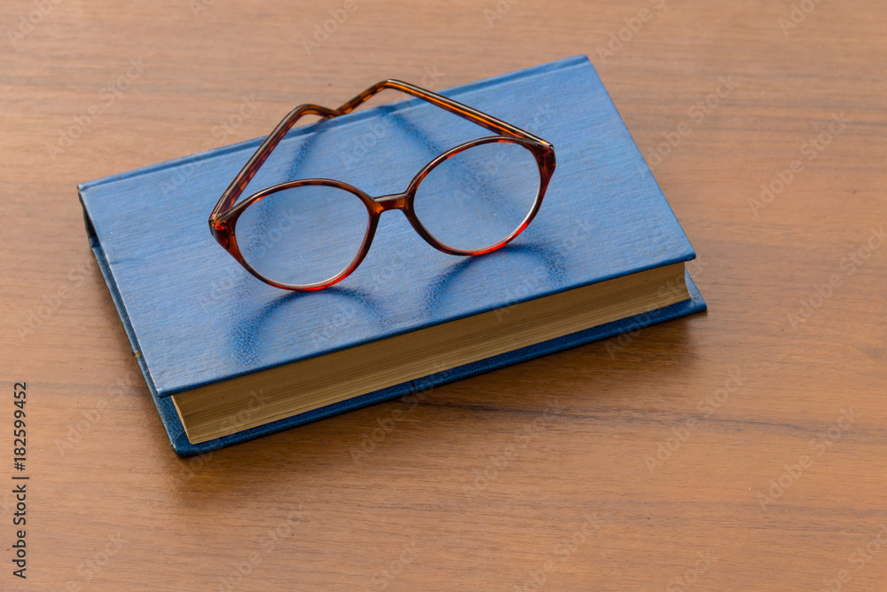 Closed book and eyeglasses on wooden background Closed book and eyeglasses on wooden background