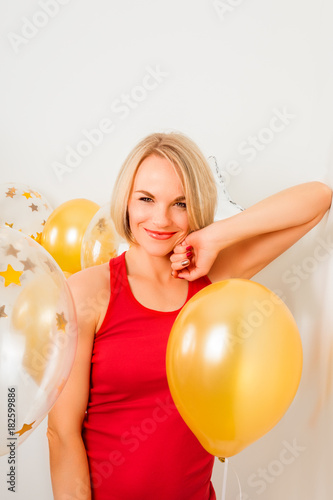 Young blonde woman in red t-shirt is smiling at the background of golden balloons. Celebrating the New Year, Christmas, Birthday Party. Close up © LALSSTOCK