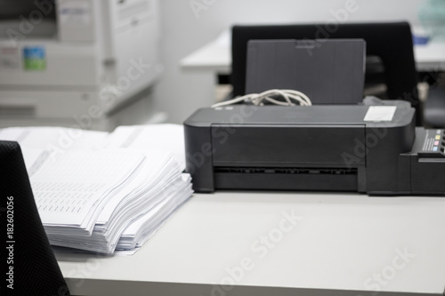 Pile of unfinished documents placed on desk with printer and copying machine.