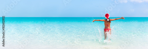 Christmas Caribbean beach tropical Santa Claus woman Happy swimming in blue ocean water panorama banner. Bikini girl with pen arms freedom carefree. Travel vacation holidays under the tropical sun.