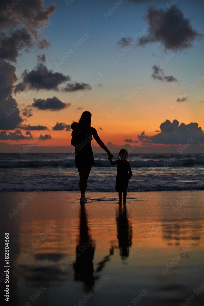 silhouette of mother carrying daughters front of beautiful ocean beach sunset