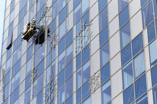 Mounting illuminating snow flakes on modern building with a help of construction cradle. Skyscraper glass wall with big artificial snowflakes and hanging construction cradle