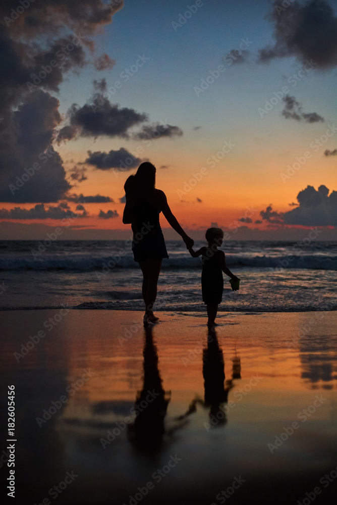 Fototapeta premium silhouette of mother carrying daughters front of beautiful ocean beach sunset