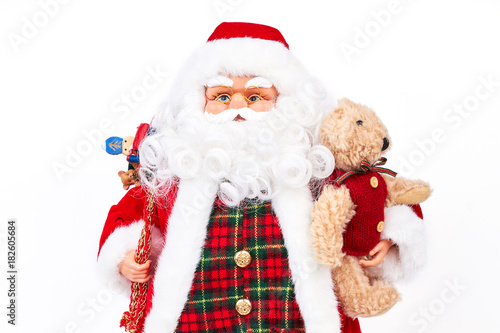 Studio portrait of Santa Claus doll with presents. Studio shot of cute grandfather frost holding plush teddy bear isolated on white background. Traditional symbol of New Year and Christmas. © DenisProduction.com