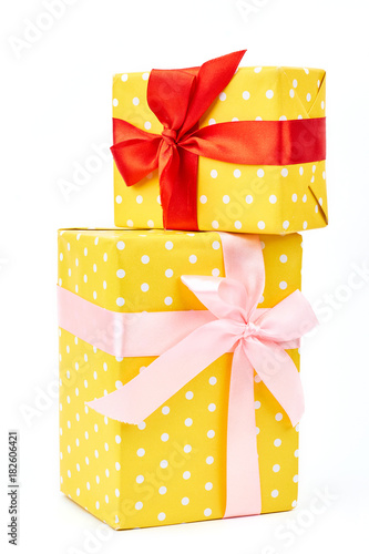 Two yellow dotted gift boxes. Presents are packed in colored paper. Polka-dot pattern tied with a beautiful pink and red ribbons over white background.