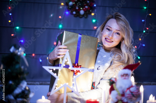 Gorgeous young woman with a gift box in her hands in christmas decorated room. Happiness and holiday spirit