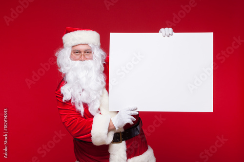Santa Claus pointing in blank advertisement banner isolated on red background with copy space © satyrenko