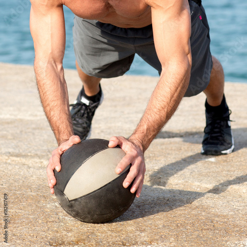 Athletic man making push ups on medicine ball near the sea