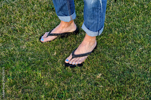 Two female feet walking across green grass in flip flops