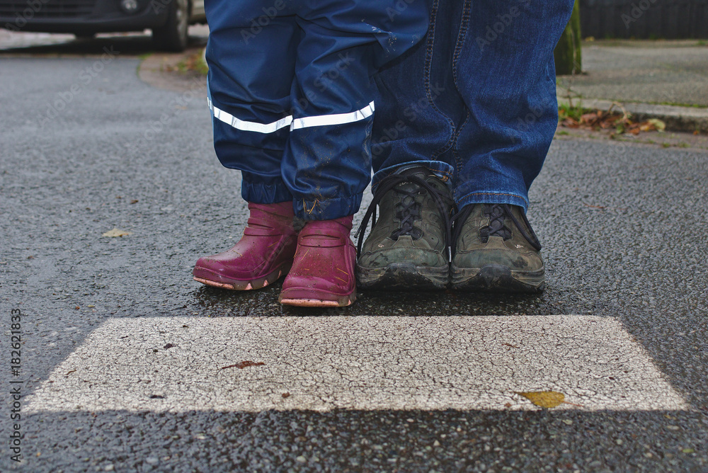 Parent and child waiting at the cross walk, shown from the knee down Parent and child waiting at the cross walk, shown from the knee down