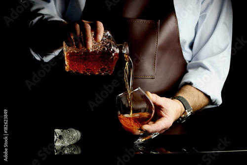 мужчина наливает коньяк в бокал за барной стойкой