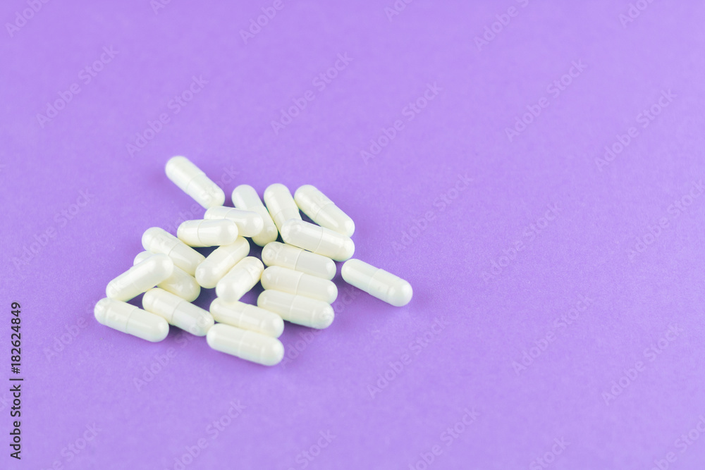 Close up white capsules on purple background with copy space. Focus on foreground, soft bokeh. Pharmacy drugstore concept Close up white capsules on purple background with copy space. Focus on foreground, soft bokeh. Pharmacy drugstore concept