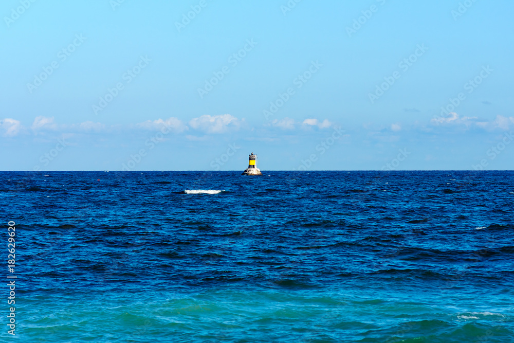 Seascape. Blue sea and sky. In the background a small lighthouse.