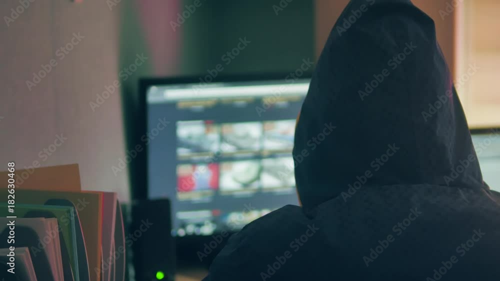 Male hacker internet working on a computer. man indoor hacker in hood hiding his Internet face Male hacker internet working on a computer. man indoor hacker in hood hiding his Internet face