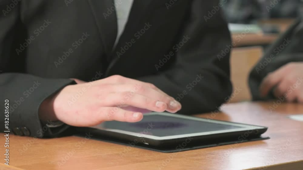 Close-up of hand of student boy dressed in black suit sits at desk at office the resting and looking at favorite photos using the screen of computer tablet in white-black colour. Close-up of hand of student boy dressed in black suit sits at desk at office the resting and looking at favorite photos using the screen of computer tablet in white-black colour.