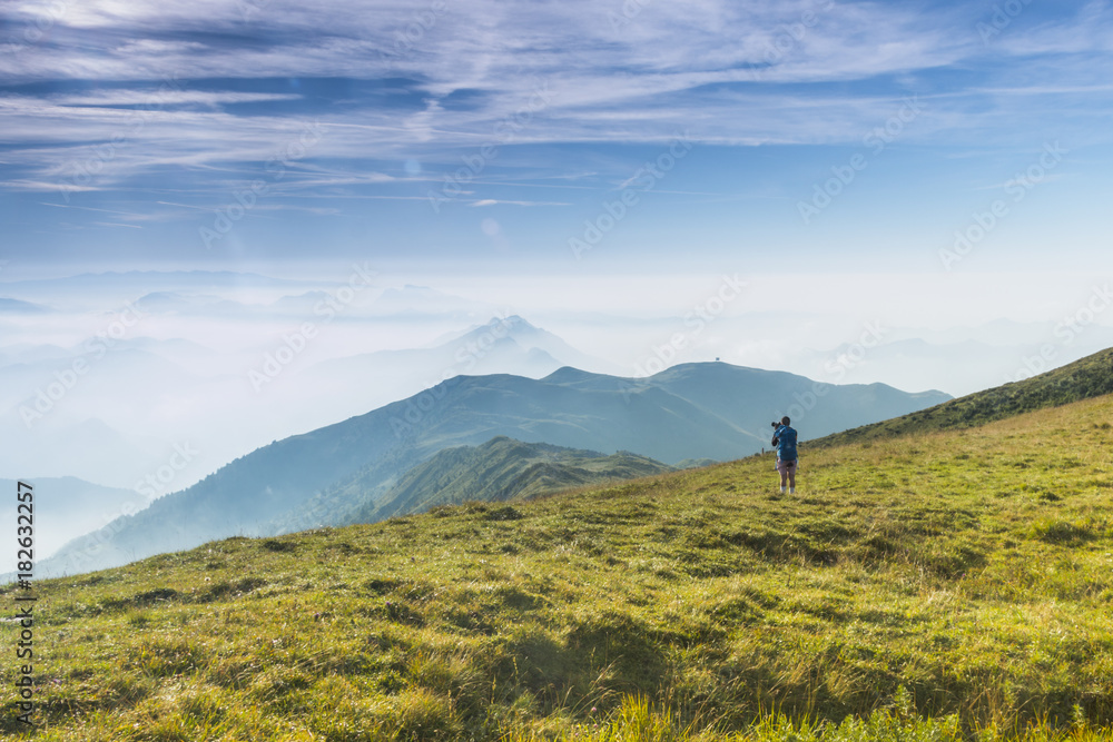 A hiker admiring and watching a foggy mountain view, Brescia province, Lombardy district, Italy
