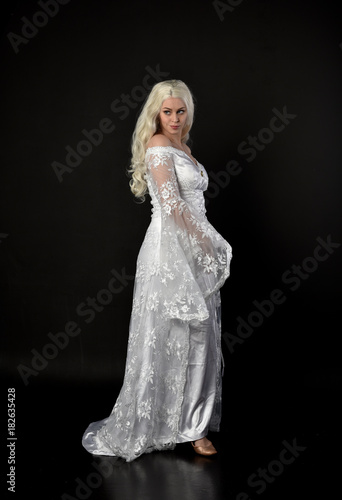 full length portrait of a blonde lady wearing beautiful lace gown  standing pose on black background.