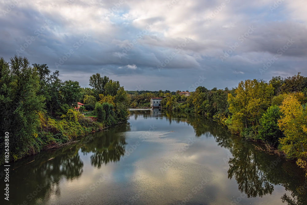 River with reflections of green trees under blue skies with fluf River with reflections of green trees under blue skies with fluf