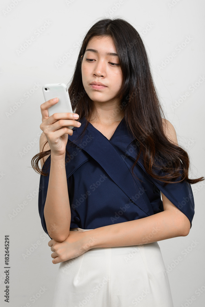 Portrait of young beautiful Asian woman using mobile phone against white background Portrait of young beautiful Asian woman using mobile phone against white background
