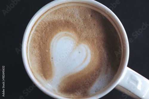 Close up image of hot coffee with heart latte art in white mug and black background