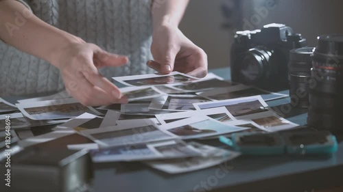 Woman with instant print transfer pictures in hands. looking at polaroid photos of road trip in dark room. table with photos, lens, photo camera.