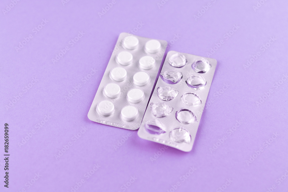 Full and empty packs of white pills packed in blisters with copy space on purple background. Focus on foreground, soft bokeh Full and empty packs of white pills packed in blisters with copy space on purple background. Focus on foreground, soft bokeh