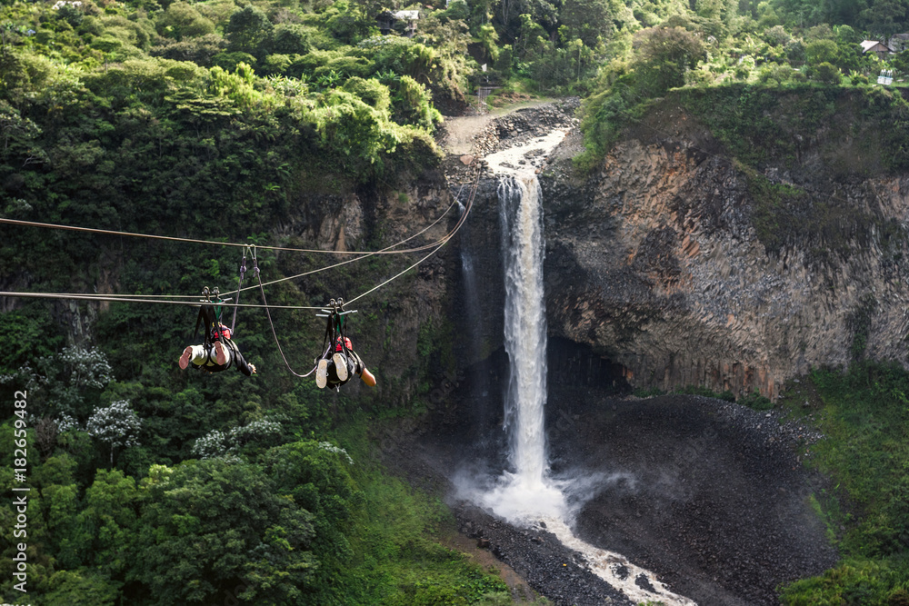 Fototapeta premium Tourists gliding on the zip line trip against Bridal veil (Manto de la novia), waterfall in Cascades route, Banos, Ecuador