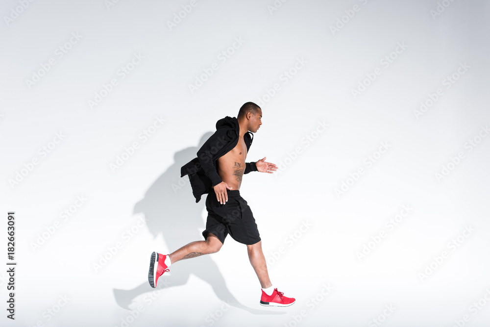 side view of young african american man in sportswear running on grey