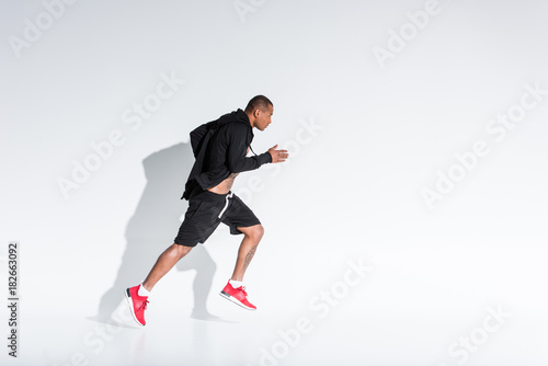 side view of young african american sportsman in sportswear running on grey © LIGHTFIELD STUDIOS