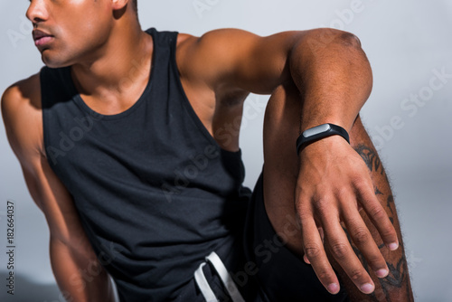 cropped shot of young african american sportsman wearing fitness tracker on grey