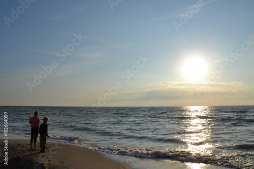 Zwei Kinder stehen beim Sonnenuntergang am Strand und schauen zum Meer © Claudia Evans 
