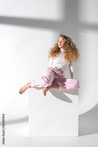 Fototapeta Naklejka Na Ścianę i Meble -  beautiful girl sitting on white cube and looking away