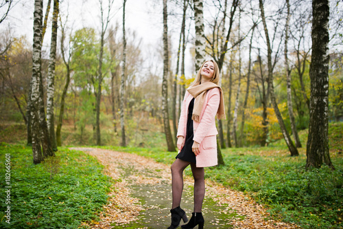 Young blonde girl at pink coat posed on autumn park.