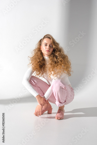 Vászonkép beautiful girl with curly hair squatting and looking at camera