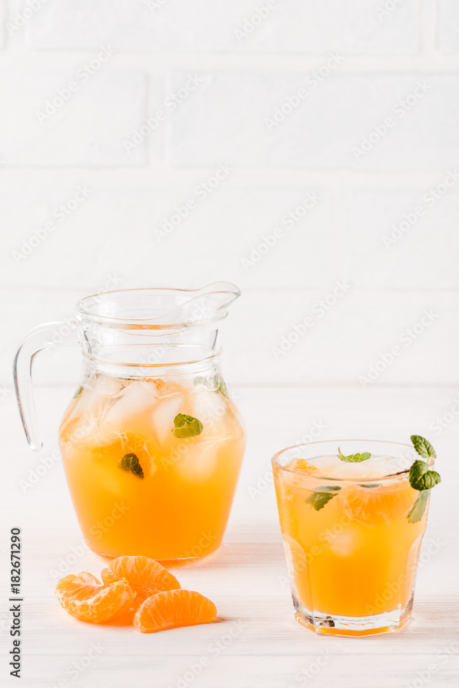 Mandarin cocktail with ice and mint in beautiful glasses and jug, fresh ripe citrus on white wooden background. Sweet orange juice. Close up photography. Selective focus Mandarin cocktail with ice and mint in beautiful glasses and jug, fresh ripe citrus on white wooden background. Sweet orange juice. Close up photography. Selective focus