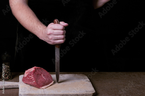 Butcher preparing to cutt raw beaf meat on kitchen. Copy space photo