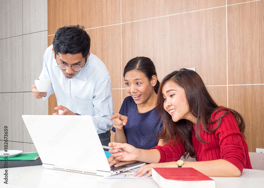 Group of young asian business woman/man working with happy feeling and smile in the office, sitting on desk with computer laptop reading good news and feeling surprise. Group of young asian business woman/man working with happy feeling and smile in the office, sitting on desk with computer laptop reading good news and feeling surprise.