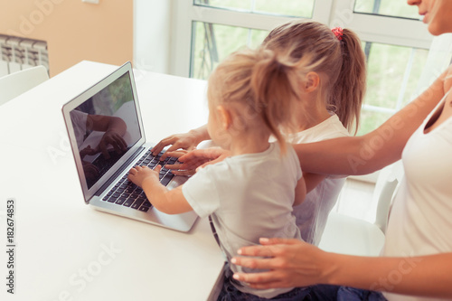 Young happy family using laptop while sitting at kitchen at home. Little children girl watching cartoons with parents