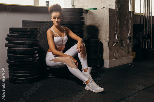 Fit power athletic confident young woman crossfit trainer doing exercises with heavy weight barbell plate in gym rising hand. Fitness muscular body, strong hand on dark background Pumping up muscles