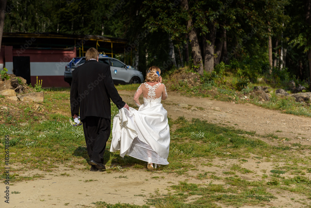 Fototapeta premium Bride and groom walking away in summer park outdoors