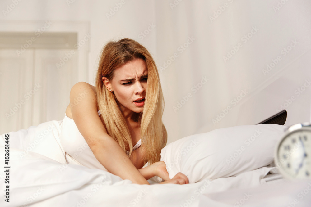 Tired blonde lady hates the clock while she wakes up