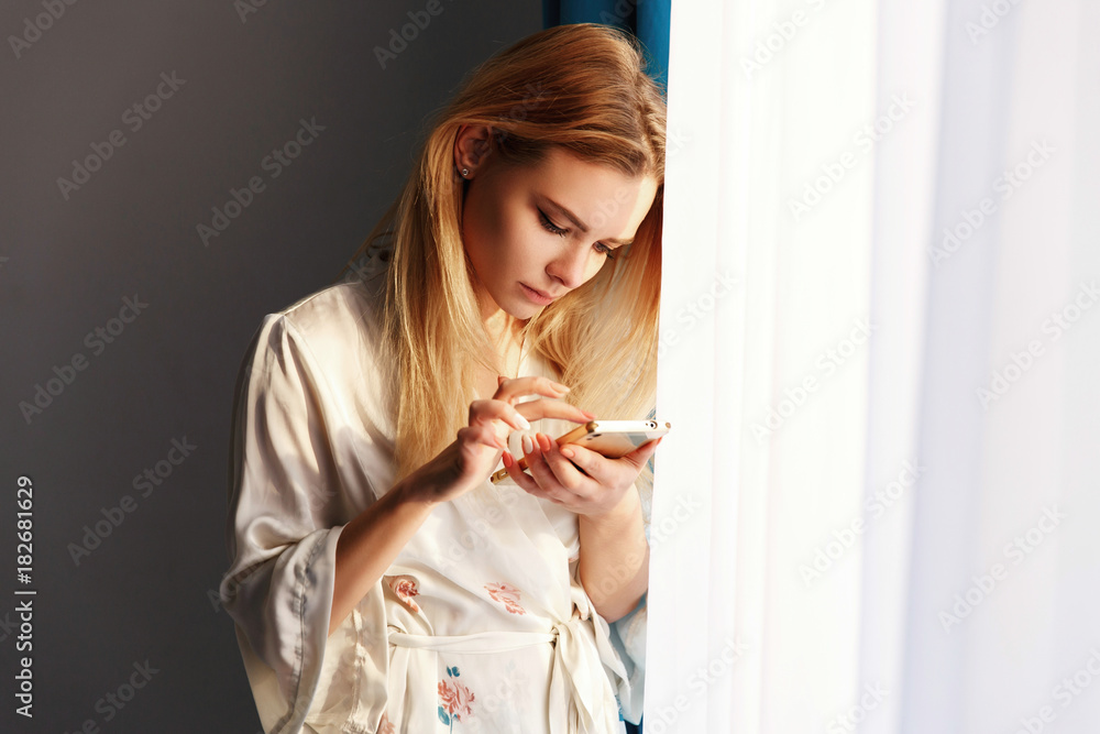 Blonde Girl Checks Her Phone Standing Before The Bright Window Stock 写真