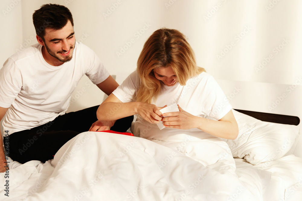 Brunette man gives to his woman a gift while she lies in the bed in the morning Brunette man gives to his woman a gift while she lies in the bed in the morning
